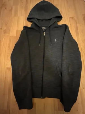 Mörkgrå hoodie från Polo Ralph Lauren - Snygg mörkgrå hoodie från Polo Ralph Lauren med dragkedja framtill och klassisk huva. Har används 2-4 gånger så den är som ny då jag köpte den i Februari. Kom gärna med frågor och vi kan diskutera priset lite grann med en snabb försäljning!
