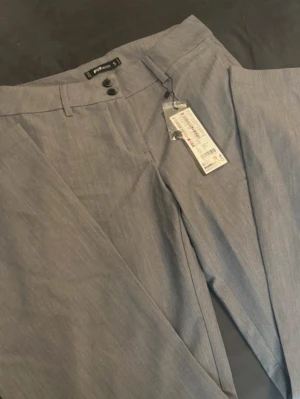 Grå kostymbyxor - Snygga grå kostymbyxor från Pull&Bear med raka ben och två knappar i midjan. Byxorna har bälteshällor och klassisk passform, perfekta för en clean och stilren look. Materialet är lätt och känns bekvämt hela dagen.