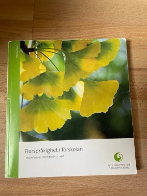 Flerspråkighet i förskolan bok - Boken 'Flerspråkighet i förskolan – ett referens- och metodmaterial' riktar sig till personal och skolledare i förskolan. Omslaget är grönt och vitt med ett foto av gula blad. Innehåller tips, erfarenheter och teori om flerspråkighet.