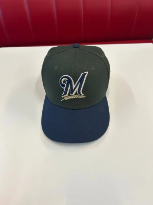 Milwaukee Brewers keps New Era grön/blå - Snygg keps från New Era med Milwaukee Brewers-logga broderad framtill. Kepsen är mörkgrön med mörkblå skärm och har klassisk form med böjd skärm. Tillverkad i slitstarkt tyg, perfekt för dig som gillar sportig stil.