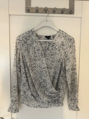 Mönstrad omlottblus från Lindex - Snygg omlottblus från Lindex i vitt med svart abstrakt mönster. Blusen har långa ärmar och ett avslappnat fall. Tillverkad i ett lätt och luftigt material. 😍