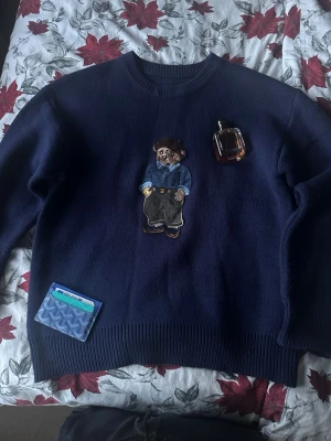 Mörkblå tröja med nallepatch - Mörkblå stickad tröja med en stor broderad nallepatch på bröstet. Kommer faktiskt inte ihåg från vilken märke jag köpte för den lappen är borta medan det skulle tvättas, och är 40% merino ull och 60% bomull, använt 2 gånger 