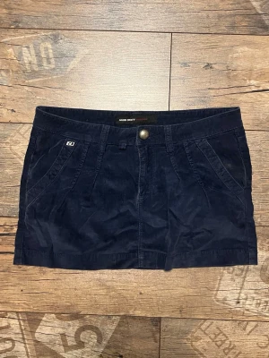 Vintage lågmidjad minikjol från Miss Sixty - Kort mörkblå minikjol från Miss Sixty i mjuk manchester. Kjolen har fickor fram och bak, bälteshällor och knappstängning framtill. Perfekt för dig som gillar en enkel men snygg look.