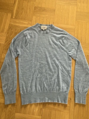 Ljusblå stickad tröja från Sandö - Ljusblå stickad tröja från Sandö med rund halsringning och ribbade muddar vid ärmslut och nederkant. Tröjan har en enkel och clean design som passar perfekt till jeans eller kjol. Materialet ser ut att vara mjukt och tunt, vilket gör den skön att bära.