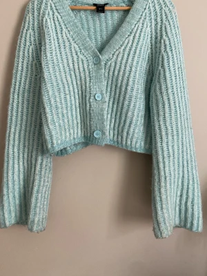 Ljusblå stickad kofta med knappar - Mysig ljusblå stickad kofta med tre stora matchande knappar framtill. Koftan har en croppad passform, bred ribbstickning och långa, lite vidare ärmar. Är i st s men passar xs och m. Säljer då den tyvärr inte kommer till användning ❤️.