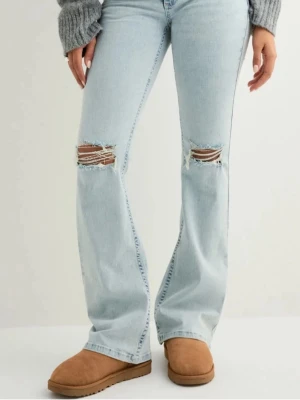 Ljusblå bootcut jeans med slitningar från Nelly - Säljer ett par ljusblå bootcut jeans med slitna knän och broderade detaljer på bakfickorna. Jeansen har hög midja och är tillverkade i klassisk denim. Perfekta för en avslappnad och trendig look.