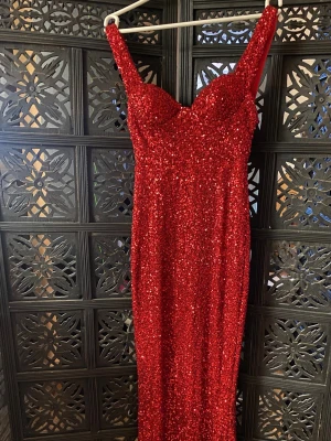 Balklänning  - Säljer en röd långklänning med glittriga paljetter och figurnära passform. Kläningen har djup urringning och öppen rygg. Perfekt för dig som vill sticka ut på bal eller fest.Använd en gång då det va min bal. 