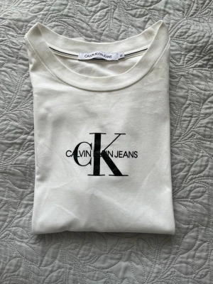 Vit Calvin Klein Jeans t-shirt - Snygg vit t-shirt från Calvin Klein Jeans med klassisk logga i svart på bröstet. T-shirten har rund halsringning och korta ärmar. Tillverkad i mjuk bomull för en skön känsla och enkel stil. Den är endast använd 1-2 gånger och därför mycket bra skick. Nästan som ny