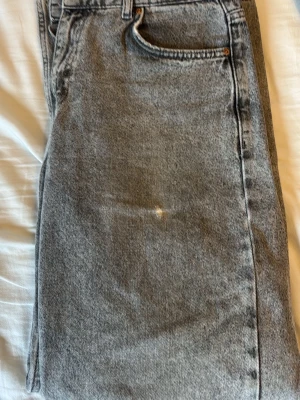 Grå tvättade raka jeans - Säljer ett par snygga grå tvättade jeans med rak passform och klassiska fem fickor. Jeansen har en vintagekänsla och är tillverkade i kraftig denim. Perfekta för dig som gillar en avslappnad och trendig stil.