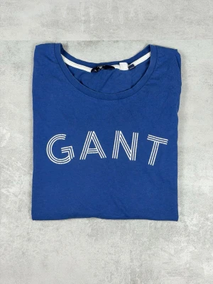 Blå GANT t-shirt med tryck - Snygg blå t-shirt från GANT med stort vitt logotryck framtill. Klassisk rund halsringning och normal passform. Tillverkad i mjuk bomull som känns skön mot huden. Perfekt för dig som gillar stilrena och tidlösa plagg.