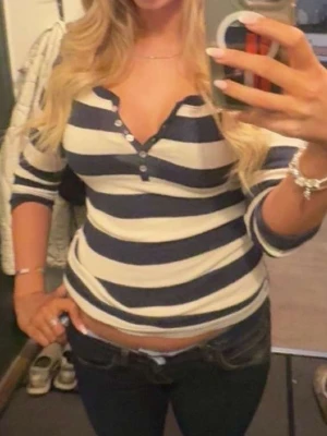 Randig v-ringad topp med knappar - Säljer en långärmad topp med breda marinblå och vita ränder. Toppen har v-ringning med knappar framtill och sitter tight. Perfekt för dig som gillar en enkel men snygg stil.