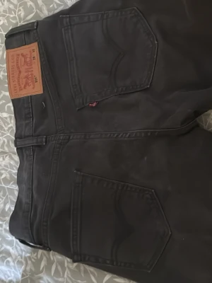  Levi's 511 jeans - Säljer ett par svarta Levi's 511 jeans med klassisk femficksdesign och dragkedjegylf. Jeansen har en slim fit passform och är tillverkade i bomull med lite stretch för extra komfort. Perfekta för en stilren och avslappnad look.