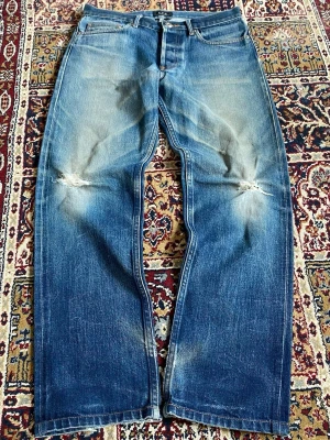 A.P.C. Blå slitna raka jeans - Säljer ett par blå jeans med raka ben och slitningar vid knäna. Jeansen har klassisk femficksdesign och tydliga tvättade detaljer för en vintagekänsla. Perfekta för en avslappnad och trendig look.