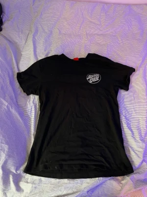 Svart Santa Cruz t-shirt - Snygg svart t-shirt från Santa Cruz med logga tryckt på bröstet. Klassisk passform och rund halsringning. Perfekt för dig som gillar streetwear och vill ha en enkel men stilren look.