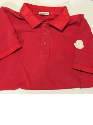 Röd pikéskjorta från Moncler - Snygg röd pikéskjorta från Moncler med klassisk krage, tre knappar framtill och Moncler-logga på ärmen. Tillverkad i mjuk bomull som känns skön mot huden. Perfekt för dig som vill ha en stilren och sportig look.(Köpt på Nk kvitto finns dock inte).