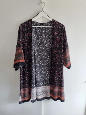 Blommig kimono Stradivarius M - Snygg kimono från Stradivarius med blommigt mönster i svart, vitt, rosa och orange. Modellen är loose fit med trekvartsärm och dekorativa bårder längst ner och på ärmarna. Perfekt att slänga över en enkel topp för en cool look. Fint skick