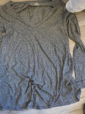 Grå långärmad tröja med v-ringning - Mjuk och enkel grå långärmad tröja med v-ringad hals. Perfekt basplagg i garderoben, tillverkad i ett tunt och stretchigt material. Passar till många olika stilar och är lätt att matcha.