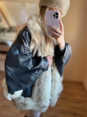 Vintage pälsjacka med skinnärmar - Unik vintage pälsjacka med fluffig beige päls och kontrasterande svarta skinnärmar. Jackan har oversized passform och bred krage, perfekt för dig som vill sticka ut. Materialmixen ger en cool retrovibe och jackan är riktigt varm för kalla dagar.