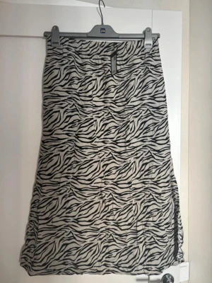 Zebramönstrad långkjol med slits - Säljer en snygg långkjol med zebramönster i svart och vitt. Kjolen har en slits på sidan som ger en extra cool detalj. Perfekt för dig som vill sticka ut lite extra. Materialet känns lätt och flowy.