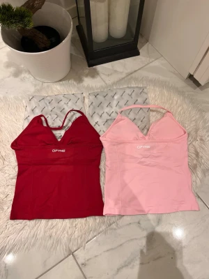 RESERVERAD ( JULII ) - Säljer två snygga linnetoppar från DFYNE, en i rött och en i ljusrosa. Winter Berry och light rose Båda har smala axelband, v-ringad hals och ärmlös design. Materialet är stretchigt och mjukt, perfekt för en trendig och bekväm look. DFYNE-logga framtill på båda topparna.