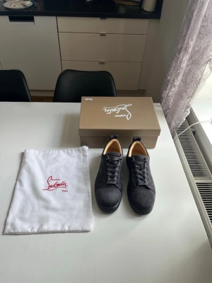 Christian Louboutin svarta sneakers - Svarta sneakers från Christian Louboutin med klassisk låg siluett och ikoniska röda sulor. Skorna har svarta skosnören och ovandel i mocka. Kommer med originalkartong och dustbag med logga.