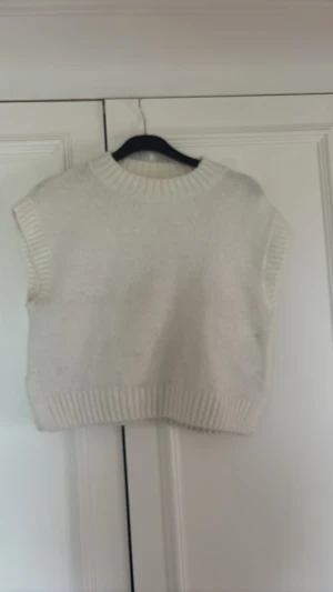 Vit stickad väst från Gina Tricot - Säljer en vit stickad väst från Gina Tricot. Västen har ribbade kanter vid hals, ärmhål och nederkant. Den är croppad och har en enkel, stilren design som passar perfekt till lager på lager-look.