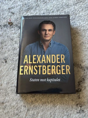 Staten mot kapitalet av Ernstberger - Säljer en signerad inbunden bok 'Staten mot kapitalet' av Alexander Ernstberger. Inbunden med svart och gul omslag, porträtt på framsidan och tydlig titel. Boken är utgiven av Mondial.