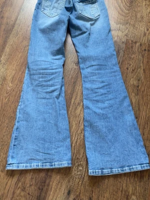 Ljusblå utsvängda jeans - Säljer ett par ljusblå jeans med utsvängda ben och snygga detaljerade bakfickor. 