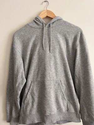 Grå basic hoodie  - En stilren grå hoodie med huva och dragsnören. Perfekt för en chill och avslappnad look. Materialet känns mjukt och bekvämt,  bomullsblandning.