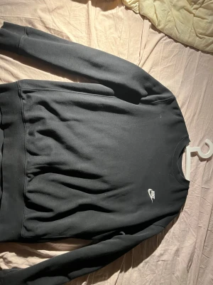 Svart Nike sweatshirt med logga - Svart sweatshirt från Nike med klassisk vit logga på bröstet. Tröjan har rund halsringning, långa ärmar och är tillverkad i mjukt material som känns skönt mot huden. Perfekt för en avslappnad och sportig stil.