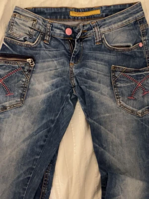 Blå jeans med rosa detaljer Cipo & Baxx - Säljer ett par blå jeans från Cipo & Baxx med slitningar och unika rosa sömmar på fickorna. Jeansen har dragkedja på ena fickan, rosa knapp och coola kontrastsömmar. Perfekt för dig som gillar y2k/2000s stil