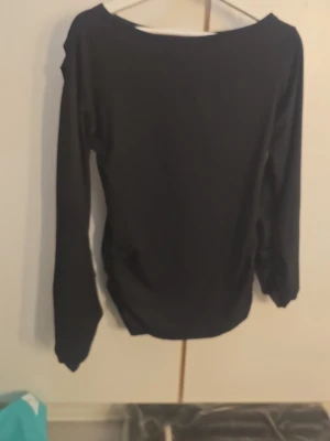 Svart långärmad topp med bred ringning - En enkel och stilren svart långärmad topp med bred ringning. Toppen har en rak passform och är tillverkad i ett mjukt, stretchigt material som sitter bekvämt på kroppen. Perfekt att matcha med jeans eller kjol för en clean look.