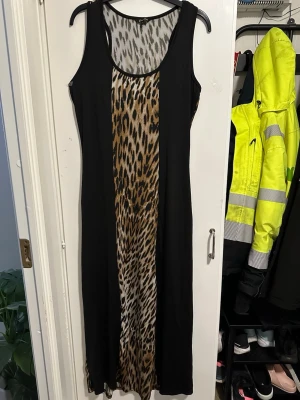 Leopardmönstrad långklänning Just Love strl: L - Cool långklänning från Just Love med leopardmönstrad mittpanel och svarta sidor. Ärmlös design och rund halsringning. Perfekt för dig som vill sticka ut med ett djurmönster. Materialet känns lätt och stretchigt.