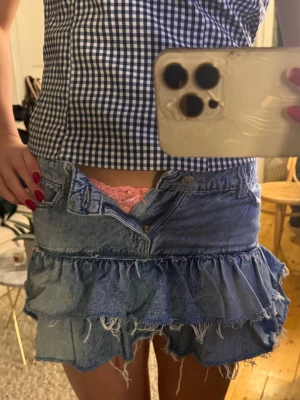 Blå jeans volangkjol - Säljer en kort jeanskjol i blå denim  med volangdetaljer och råa kanter. Kjolen har klassisk femficksdesign, bälteshällor och stängs med knapp och dragkedja framtill. Kontakta för mer bilder eller frågor💓