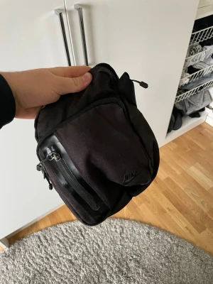 Svart axelväska från Nike - Säljer en svart axelväska från Nike med justerbar rem och flera praktiska fack med dragkedja. Väskan är tillverkad i slitstarkt tyg och har en stilren design med diskret Nike-logga på framsidan. Perfekt för att bära det viktigaste när du är på språng.