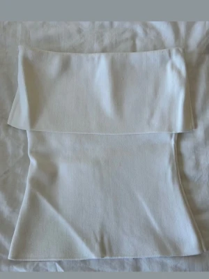 Zara vit bandeau tubtopp - Säljer en stilren vit bandeau tubtopp med ribbad struktur. Toppen är axelbandslös och har en bred kant upptill som ger en snygg offshoulder-look. Perfekt att matcha med jeans eller kjol för en clean och trendig outfit.