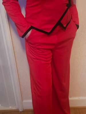 Röd cosplaydräkt med svarta detaljer - Säljer en röd maskerad- och cosplaydräkt med svarta kantdetaljer. Dräkten består av en långärmad överdel och matchande byxor med vida ben. Perfekt för dig som vill sticka ut på nästa cosplayevent eller maskerad. Materialet känns mjukt och följsamt.