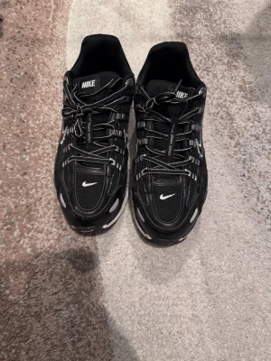 Nike p6000 - Snygga svarta sneakers från Nike med vita detaljer och reflekterande inslag. Skorna har en sportig design med mesh och syntetmaterial, samt en tjock vit sula för extra komfort. Använda ett par gånger, inga defekter
