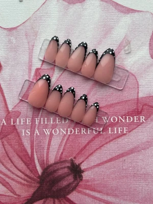 Press-on naglar med svart fransk tipp - Snygga press-on naglar i nude med svart fransk tipp och vita prickar. Mandelformade och trendiga, perfekta för dig som vill ha en cool och modern look. Kommer i set om tio naglar. Material: akryl.