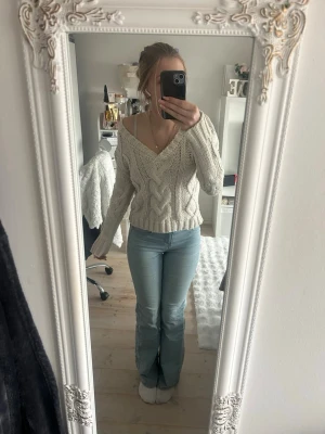 Beige kabelstickad tröja från NA-KD - Säljer en beige kabelstickad tröja från NA-KD med djup v-ringning och långa ärmar. Tröjan har ett snyggt flätmönster och ribbade muddar vid ärmslut och nederkant. 