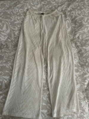 Beiga vida byxor  - Säljer ett par benvita byxor med avslappnad passform och dragsko i midjan. Byxorna har ett diskret mönster i tyget och raka ben. Perfekta för en chill och stilren look. 