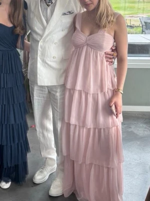 Ljusrosa volangklänning med breda axelband - En ljusrosa balklänning från Nelly som är omsydd💕Med flera lager volanger och breda axelband. Kläningen är i storlek S men är insydd i midjan, kan sprättas upp dock.