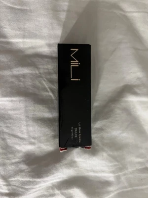 MILI Lipstick DULCE nude - Snyggt nude-färgat läppstift från MILI i nyansen DULCE. Kommer i en stilren svart och transparent hylsa med matchande svart kartong. Perfekt för dig som gillar naturliga toner och vill ha ett modernt, elegant läppstift.