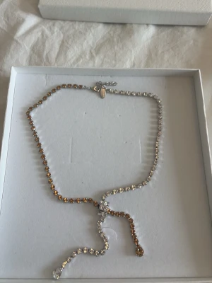 Caroline Svedbom gnistrande halsband - Säljer ett elegant halsband från Caroline Svedbom med gnistrande stenar i guld- och silverton. Halsbandet har en justerbar design och små pärlliknande detaljer som ger en lyxig känsla. Perfekt för dig som vill ha något extra till din outfit.