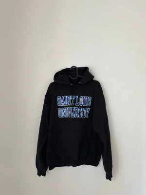 Mörkblå/svart Champion hoodie Saint Louis Univ. - Mörkblå/svart hoodie från Champion med stor vit och blå text 'Saint Louis University' på bröstet. 