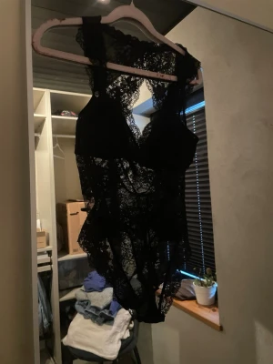 Svart spetsbody med djup rygg - Snygg svart body i genomskinlig spets med djup rygg och breda axelband. Bodyn har vackra spetsdetaljer och en feminin siluett, perfekt för att känna sig extra fin.