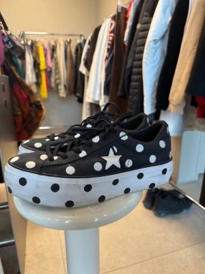 Converse med prickar  - Säljer ett par unika Converse sneakers med svart canvas, vita prickar och en vit stjärna på sidan. Skorna har tjock vit sula med prickar och klassiska svarta skosnören. Perfekt för dig som vill sticka ut med coola detaljer.