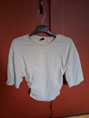 Ljusgrå croppad topp med snörning💕 - Trendig ljusgrå croppad topp med snörning i sidan och rund halsringning. Toppen har korta ärmar och är tillverkad i mjukt bomullsmaterial. Perfekt för dig som gillar en avslappnad men ändå snygg stil.