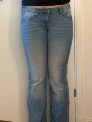 Ljusblå bootcut jeans - Säljer ett par ljusblå bootcut jeans med klassisk femficksdesign och dragkedjegylf. Jeansen har en lätt tvättad look och är tillverkade i denim med lite stretch för skön passform.