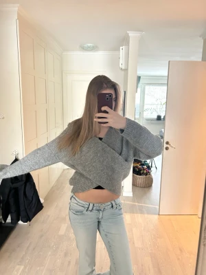 Grå omlottstickad tröja - Säljer en snygg grå stickad tröja med omlott-design och långa ärmar. Tröjan har en croppad passform och är gjord i mjukt stickat material som känns skönt mot huden. Perfekt för dig som gillar trendiga och bekväma plagg.